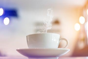 White cup of hot coffee with soft steaming on table with bokeh background at coffee shop
