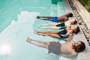 Two couple relaxing in water by the edge of swimming pool, closing eyes and enjoying shining sun