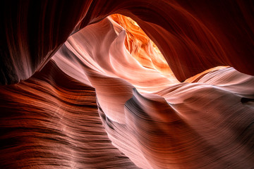 Moving towards the light of Lower Antelope Canyon in Page Arizona with natural landscapes of vibrant sandstones folded into flaky waves of fire in a narrow sandy labyrinth with caves
