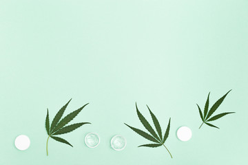 Jar with transparent cosmetic product, gel or cream with cannabis oil on green colored background. Flack with of antioxidant cream for eyes. View from above.