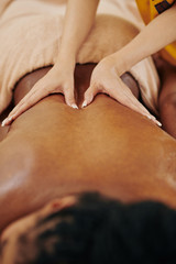 Close-up image of therapist massaging back of woman doing long gliding strokes to reduce stress