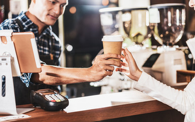 Asian Barista serving a paper cup of coffee to customer in coffee shop, Small business owner and startup in coffee shop and restaurant concept