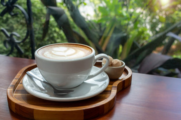 Cup of coffee on wooden tray on green garden and sunlight background. Breakfast time.