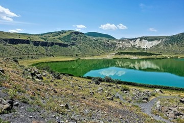 Fototapeta na wymiar Beautiful mountain lake Nar. An emerald round-shaped reservoir in the crater of an extinct volcano. Summer sunny day, blue sky, light clouds. Reflection in water. Cappadocia. Turkey. 