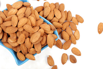 Group of almonds inside and outside bowl isolated on white.