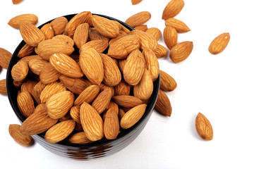 Group of almonds inside and outside bowl isolated on white.