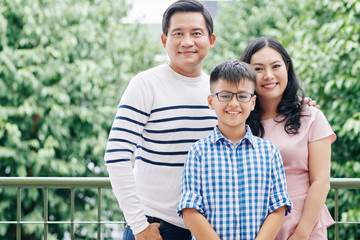Obraz premium Portrait of happy Vietnamese family with preteen child standing outdoors and looking at camera