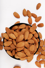 Group of almonds inside and outside bowl isolated on white.