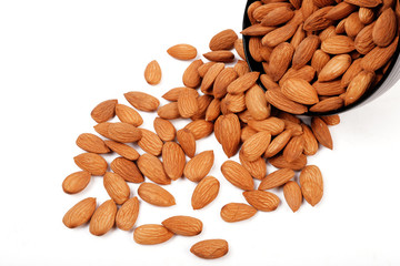 Group of almonds inside and outside bowl isolated on white.