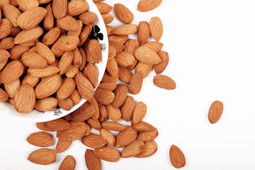Group of almonds inside and outside bowl isolated on white.