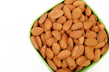 Group of almonds inside and outside bowl isolated on white.