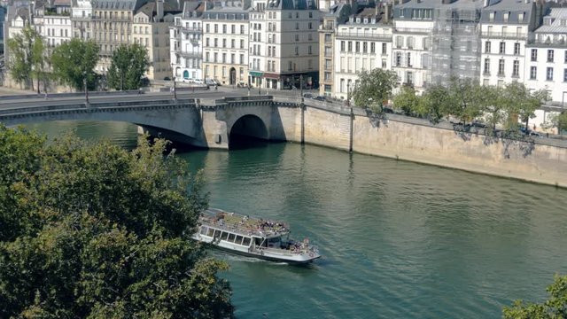 Bateau mouche boat on the Seine in Paris with trees in foreground, bridge and ile Saint-Louis in the background
