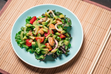 Flat lay - Asian Salad with seafood with avocado, tomatoes, octopus and mussels in blue plate on wooden table. Concept of healthy diet food.