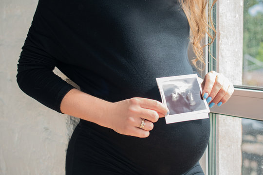 A pregnant woman in black dress holds an ultrasound image of her child: the concept of women's health