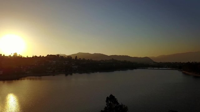 Aerial descending and panning shot of urban lake in Los Angeles during sunset. 4K