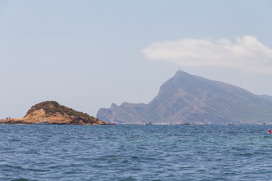 Island on the Mediterranean Sea and people enjoying a summer day of water sports and sports boats Alicante / Spain. In the background, a view of Punta Bombarda on the mountain of the Serra Gelada Natu