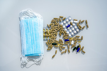 A table with several surgical masks. Assorted pharmaceutical medicine pills, tablets and capsules near the masks. High quality photo