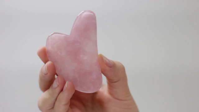 Pink quart gua sha in woman's hand on white background