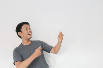 Wow and surprised face with smile of young Asian man in gray t-shirt with hand point on empty space.