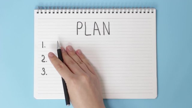 Female hand writes in notepad of goal for 2021 on blue background, top view