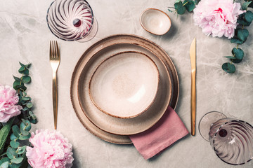 Flat lay composition with peony, eucalyptus flowers, empty plates, napkin, golden cutlery, wineglasses for serving a festive table, dinner on marble background. Copy space. Top view. Table setting