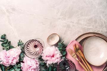 Flower arrangement on table served for festive dinner with copy space for your text, invitation. Greeting card. Top view. Peony, eucalyptus, plates, golden cutlery, wineglasses on marble background