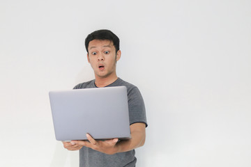 Wow face of Your Asian man shocked what he see in the laptop on isolated grey background.