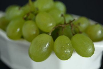 Fresh juicy green grapes on in a bowl close up on black background
