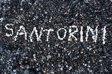 Text Santorini made of white stones on dark pebbles,  Volcanic beach at Kamari, Greece. Holidays...