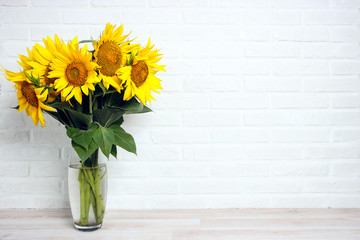 A bouquet of sunflowers in a vase against the background of a white brick wall.