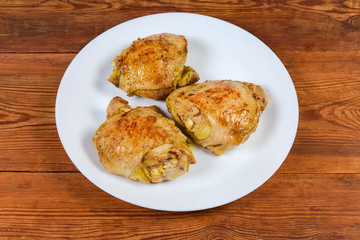 Baked chicken thighs on the white dish on rustic table