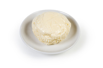 Small head of soft cheese on saucer on white background