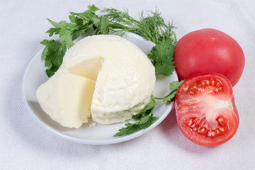Soft cheese on saucer among the tomatoes, greens on tablecloth