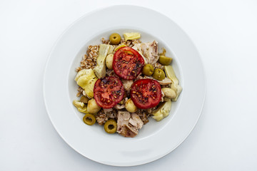Fresh summer salad with: spelled, tomatoe, olive, mushroom and artichoke in white plate. Top view