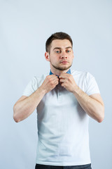 A man fastens a button on his white polo. he is on a white background. The guy is putting on a T-shirt. Facial expressions on a man's face