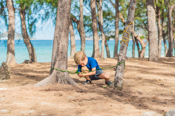 Camping people outdoor lifestyle tourists in summer forest near lazur sea. Blond serious boy in...