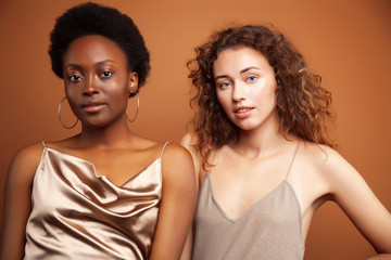 two pretty girls african and caucasian blond posing cheerful together on brown background, ethnicity diverse lifestyle people concept