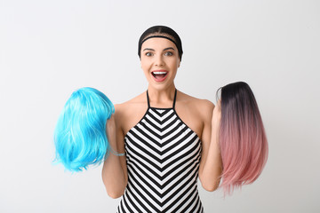 Beautiful young woman with different wigs on light background