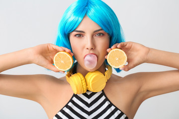 Beautiful young woman in wig, with lemon and headphones on light background