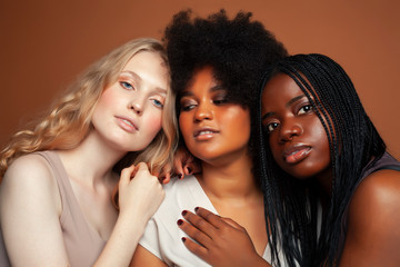 young pretty african and caucasian women posing cheerful together on brown background, lifestyle diverse nationality people concept