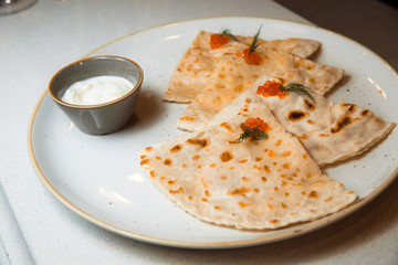 Yantyk with salmon, red caviar, served with sour cream sauce. Lies on a white, round plate.