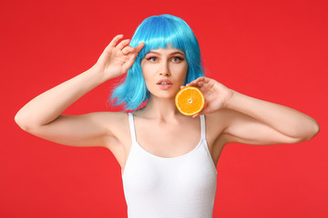 Beautiful young woman in wig and with orange on color background