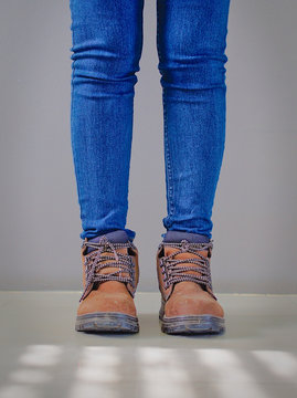 Isolated skinny legs of a lady wearing blue jeans and 
 worn safety shoe.