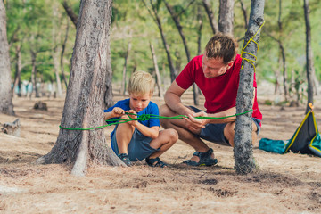 Camping people outdoor lifestyle tourists in summer forest near lazur sea. Blond boy son with...
