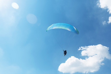 Blue Paraglider flying into the sky with clouds on a sunny day