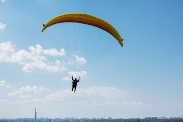 Yellow paraglider flying above the city into the blue sky with clouds on a sunny day