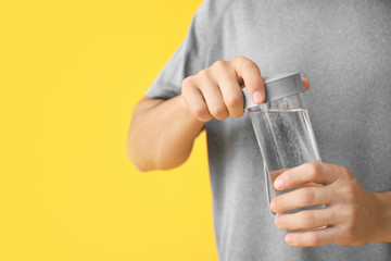 Young man with bottle of water on color background, closeup