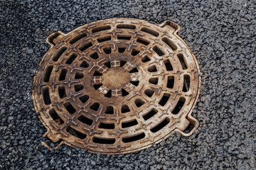 Closed sewer manhole, which is located on the sidewalk. There are holes in the manhole cover. Close up