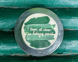 Top view of a small minimalist cake with green icing. With Tagalog words translated as 1 year and...