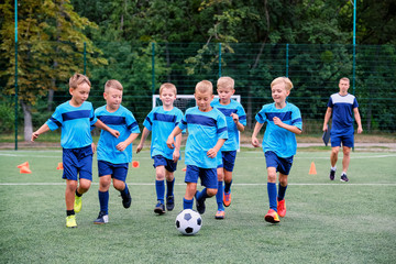 Kids running and kicking soccer ball on warming before football training session. Coach in the...